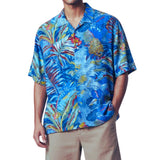 A man wearing a short-sleeve button-up Hawaiian shirt with a vibrant tropical leaf and floral print in shades of blue, red, yellow, and green, paired with khaki pants, against a plain white background.