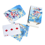 A set of illustrated playing cards with tropical designs, including palm trees, flowers, and sun motifs. One card is shown face up with red diamond symbols, and the deck and box are arranged on a plain white background.