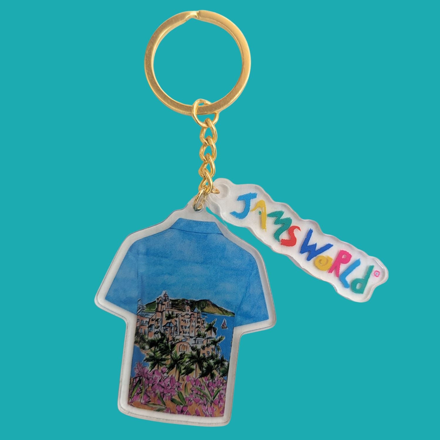 A Jamsworld acrylic keychain featuring a t-shirt-shaped charm with a colorful landscape illustration and a separate acrylic tag with the Jamsworld logo in multicolored letters, attached to a gold-tone split ring on a solid teal background.