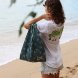 Person on a beach holding a green patterned bag and white shirt with a design.