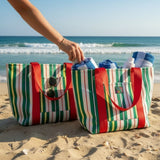 Two striped beach bags on sand with ocean in background