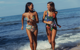 Two women in colorful swimsuits walking on a beach with ocean waves in the background