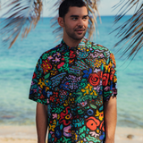 Man wearing a colorful patterned shirt on a beach with palm leaves and ocean in the background