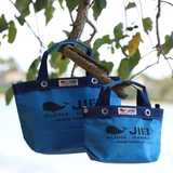 Two blue JIB bags hanging on a tree branch with green leaves in the background.