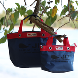 Two blue bags with red straps hanging from a tree branch outdoors.
