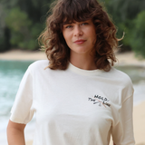 Woman wearing a white t-shirt with text, standing outdoors near water.