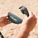 Person holding a green sunglasses case with 'Jaws World' branding against a blurred natural background.