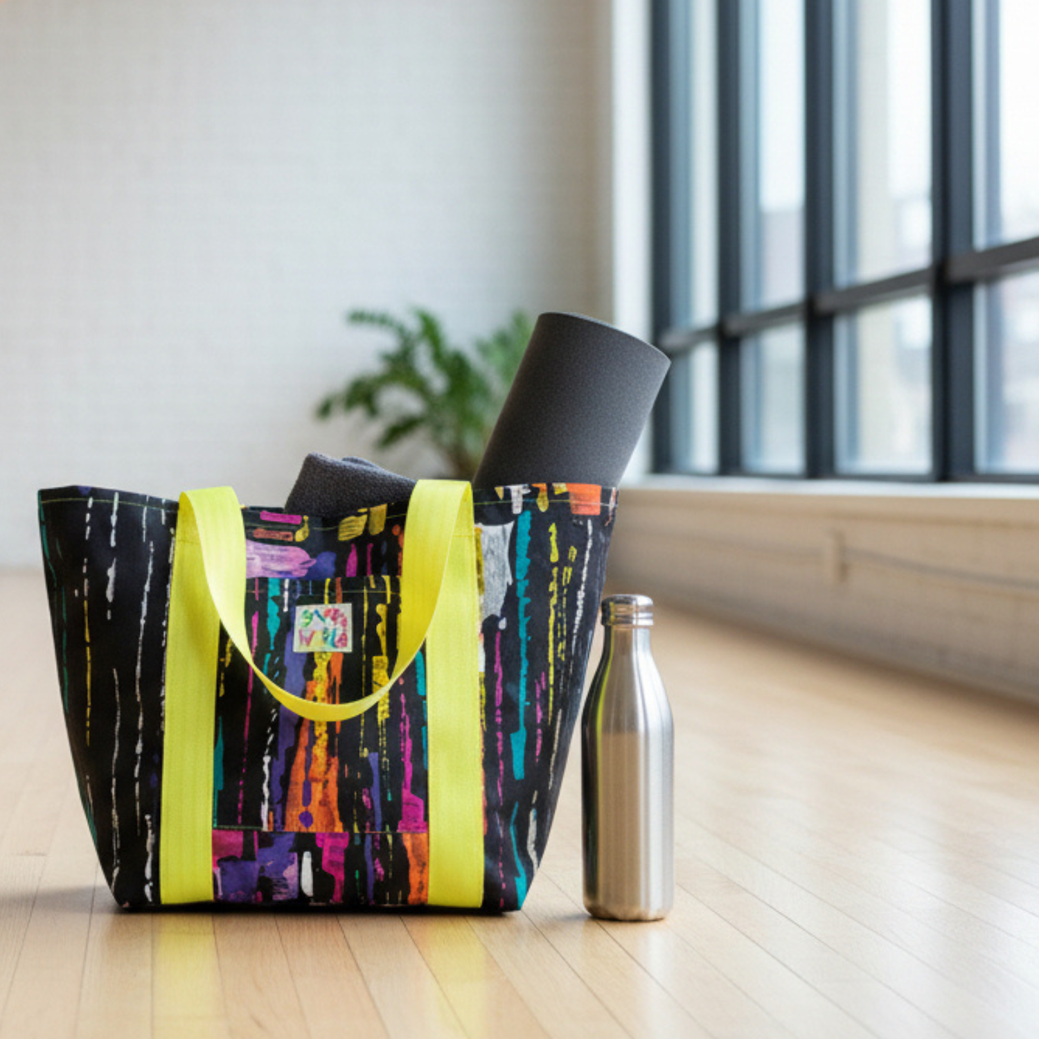 Colorful tote bag with a yoga mat and water bottle on a wooden floor.