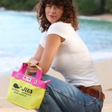 Woman sitting on a beach holding a yellow and pink bag with 'JIB' branding.