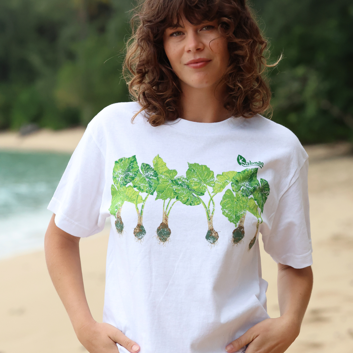 Person wearing a white t-shirt with green leaf design on a beach