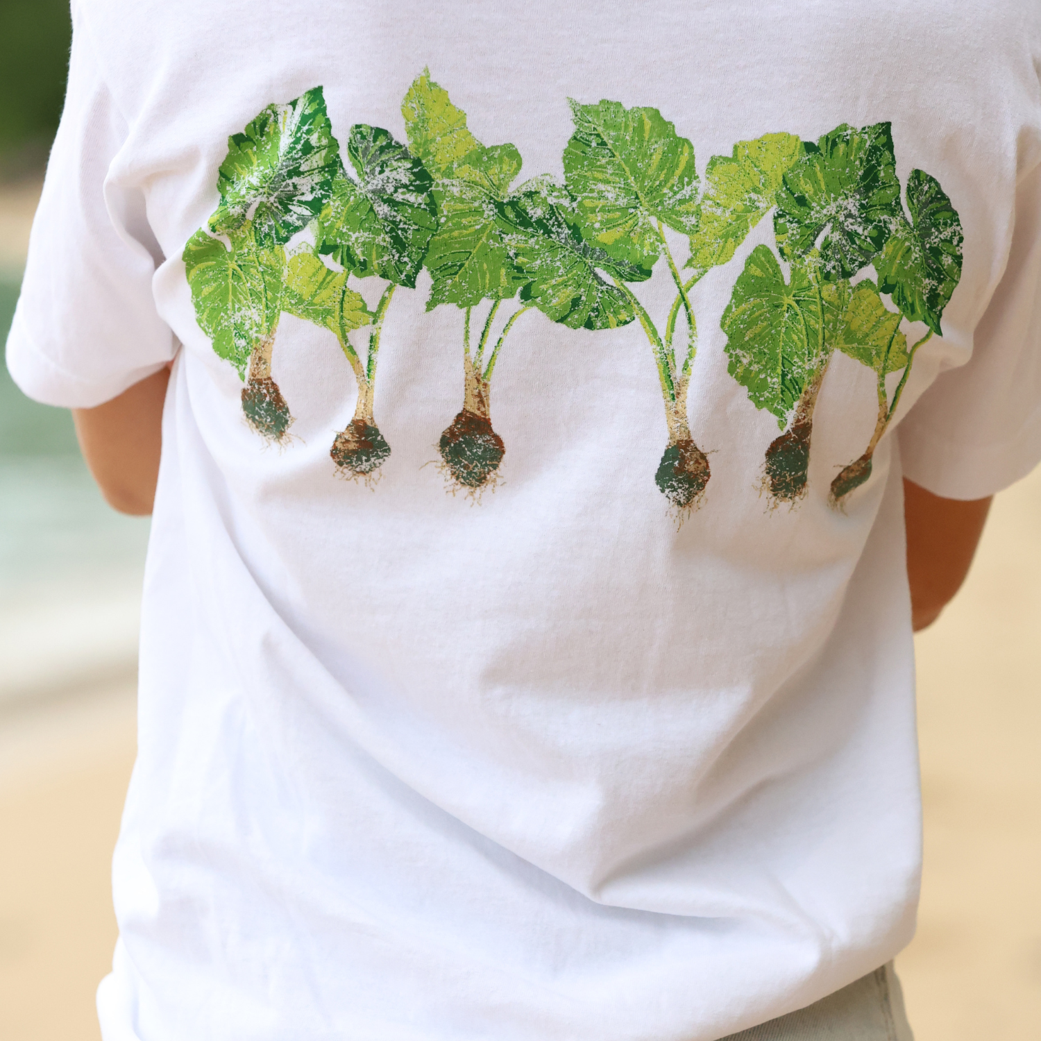 White t-shirt with green leaf design on a blurred natural background