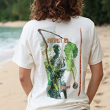 Person wearing a white t-shirt with a graphic design on the back, standing on a beach.