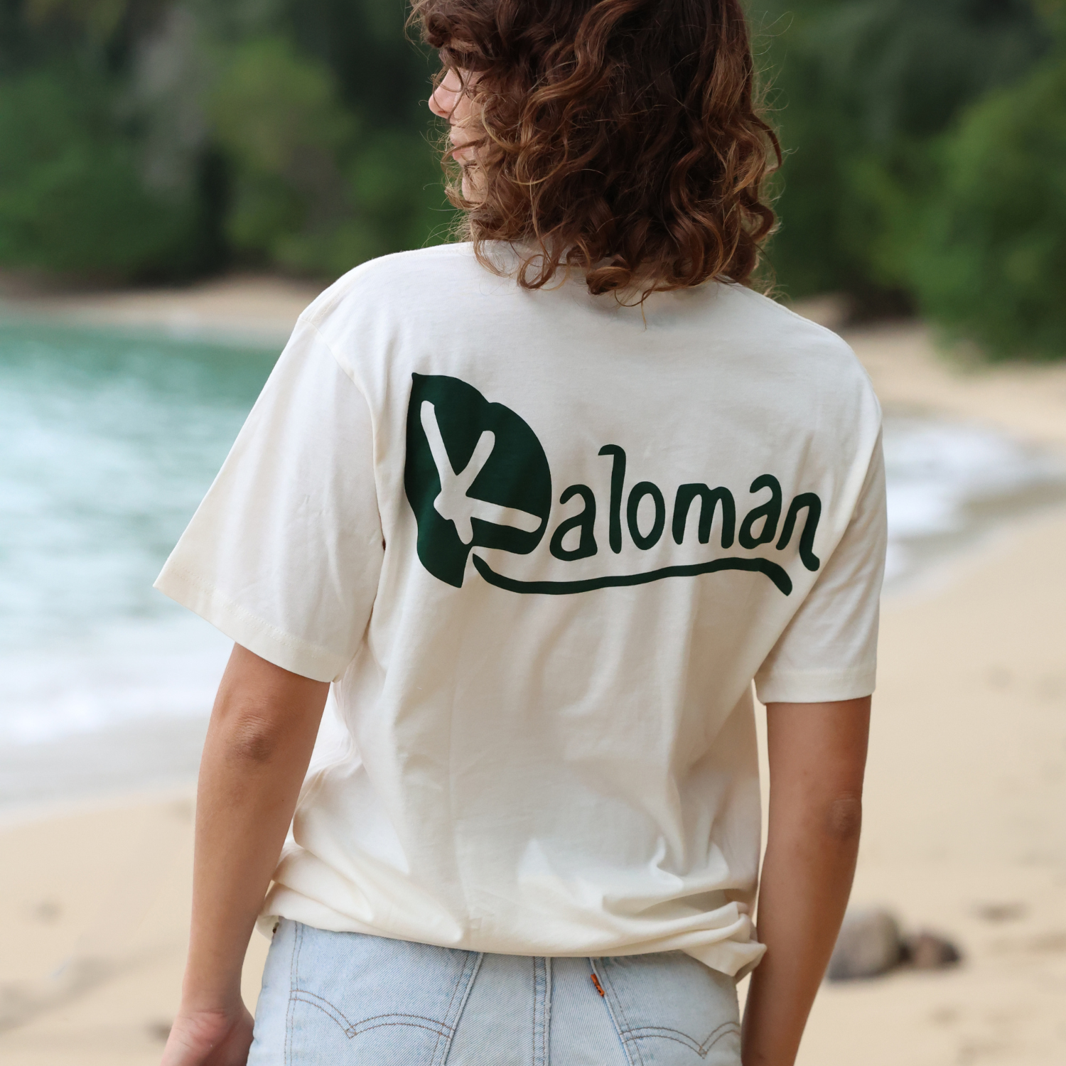 Person wearing a white t-shirt with 'Valoman' logo on a beach