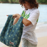 Person holding a green patterned bag by a body of water