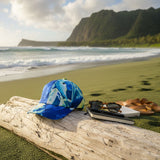 Blue cap on a log with sunglasses and notebook on a beach with cliffs in the background