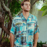 Man wearing a colorful patterned shirt standing outdoors with greenery in the background